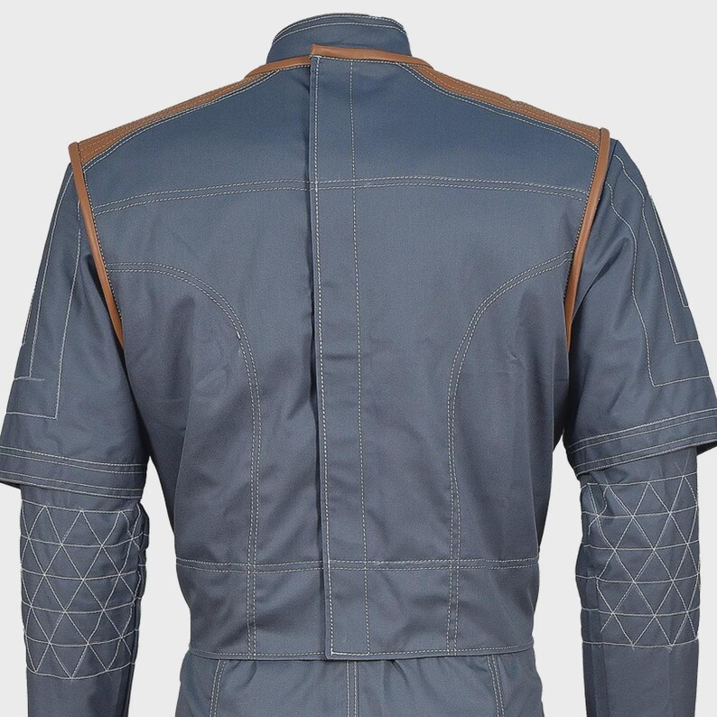 May include: A slate blue jacket featuring brown leather-like trim along the shoulders and upper back. The garment includes a high collar, visible white topstitching, and a geometric triangular quilted pattern on the lower sleeves and cuffs.
