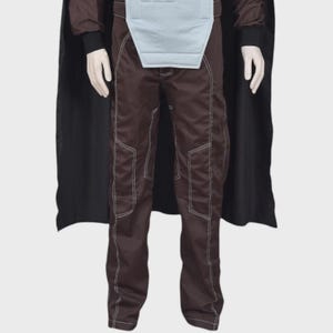 May include: A dark brown costume set featuring long trousers with prominent white topstitching, a light gray chest panel, and a long black cape. The trousers have a structured fit with visible seam lines running down the legs and dark sleeves.