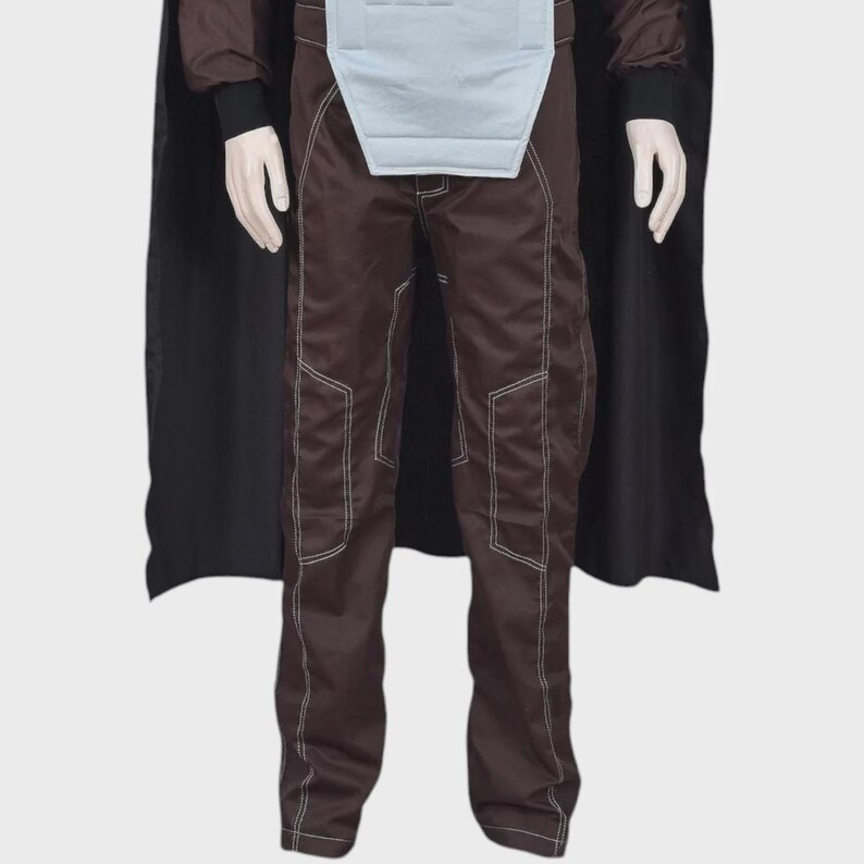 May include: A dark brown costume set featuring long trousers with prominent white topstitching, a light gray chest panel, and a long black cape. The trousers have a structured fit with visible seam lines running down the legs and dark sleeves.