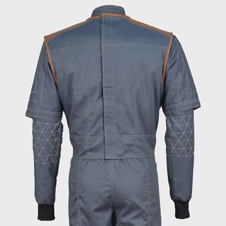 May include: A slate blue jacket with brown leather-like shoulder accents and white contrast stitching. The sleeves feature a quilted triangular pattern on the forearms, a high collar, and black ribbed cuffs. The back displays a vertical center seam.