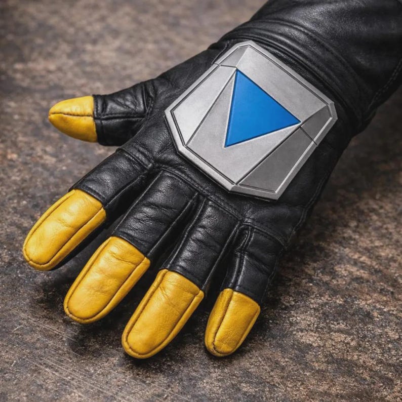 May include: A black leather glove featuring yellow leather fingertips and a large, silver-toned metallic plate on the back of the hand. The plate is shaped like a shield and contains a prominent, inverted blue triangle centered within its design.