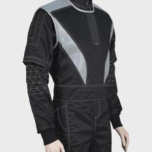 Puede incluir: Un mono negro con cuello alto y un chaleco sin mangas superpuesto con paneles acolchados de color gris plateado. Las mangas largas tienen un patr&oacute;n geom&eacute;trico de tri&aacute;ngulos blancos en los antebrazos y costuras blancas en toda la prenda.