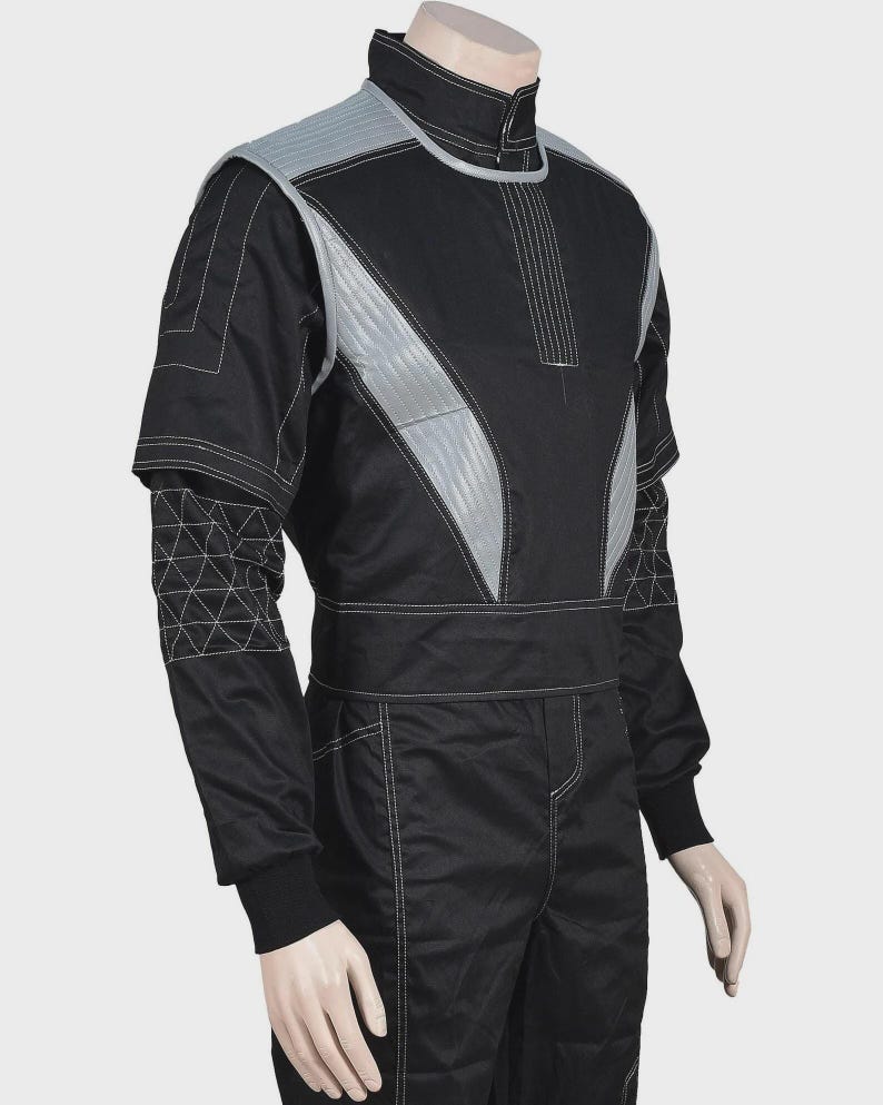 Puede incluir: Un mono negro con cuello alto y un chaleco sin mangas superpuesto con paneles acolchados de color gris plateado. Las mangas largas tienen un patr&oacute;n geom&eacute;trico de tri&aacute;ngulos blancos en los antebrazos y costuras blancas en toda la prenda.
