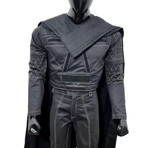 May include: A black long-sleeved tactical jacket and matching trousers set featuring white contrast stitching, geometric grid patterns on the sleeves, a wrap-style chest overlay, integrated black velcro panels, and a long black cape attached at the shoulders.