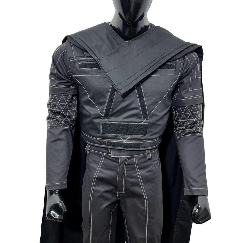 May include: A black long-sleeved tactical jacket and matching trousers set featuring white contrast stitching, geometric grid patterns on the sleeves, a wrap-style chest overlay, integrated black velcro panels, and a long black cape attached at the shoulders.