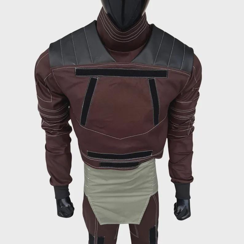 Puede incluir: Una chaqueta marr&oacute;n de manga larga con cuello alto, paneles negros en los hombros y tiras de velcro horizontales negras en el pecho. La chaqueta presenta costuras blancas en contraste y un panel de cintura en color verde oliva claro.