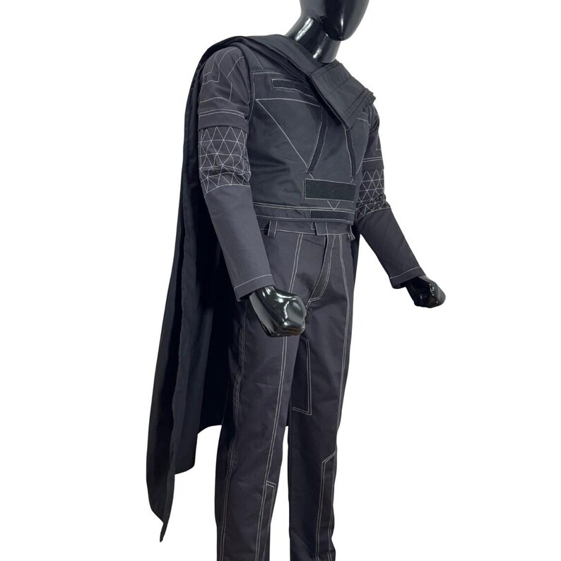 May include: A dark gray costume set featuring a long cape, a long-sleeved top with geometric white line patterns on the sleeves, and matching trousers. The ensemble includes visible white stitching details throughout the fabric and a structured collar.