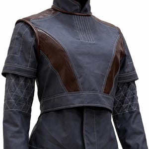 May include: A dark grey jacket with a high collar and brown leather-like shoulder panels. The sleeves feature a quilted diamond pattern with white stitching. The jacket has a structured, layered design with visible white topstitching throughout.