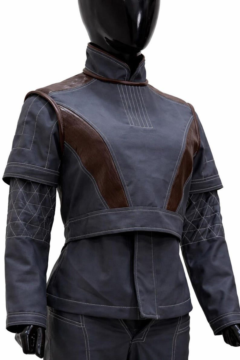 May include: A dark grey jacket with a high collar and brown leather-like shoulder panels. The sleeves feature a quilted diamond pattern with white stitching. The jacket has a structured, layered design with visible white topstitching throughout.