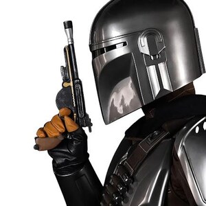 May include: A metallic silver helmet with a T-shaped visor, worn with dark armor featuring a bandolier of small cylinders. A black and gold blaster pistol is held in a gloved hand, with the armor plates reflecting light against a white background.