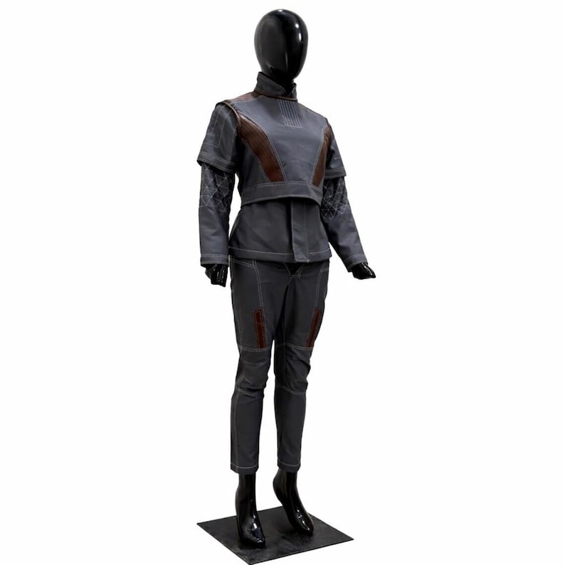 May include: A grey two-piece outfit consisting of a high-neck top with brown shoulder panels and long sleeves featuring a diamond-stitched pattern, paired with matching grey trousers that have brown accents and visible white stitching throughout.
