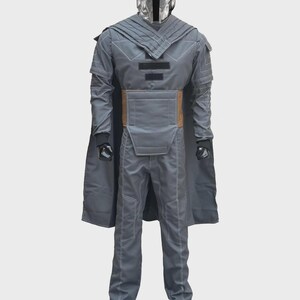 Puede incluir: Un disfraz gris de cuerpo completo que presenta una capa larga, una pieza de pecho estructurada con detalles rectangulares negros y un panel de cintura color canela. El conjunto incluye mangas largas con costuras visibles, pantalones grises a juego y un casco plateado.