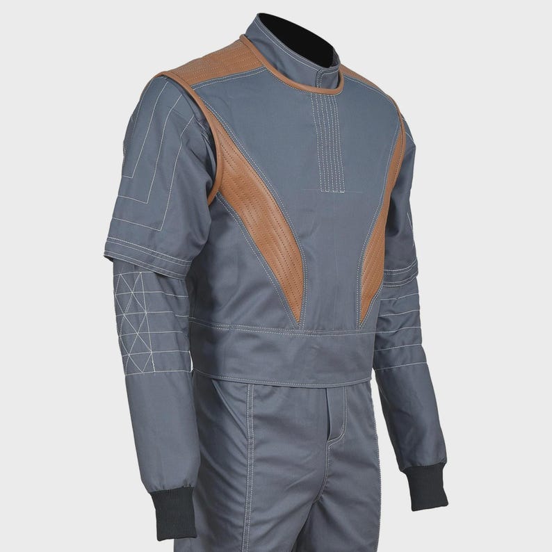 May include: A grey jumpsuit featuring tan leather-like panels on the chest and shoulders. The garment includes a high collar, long sleeves with white stitched grid patterns on the forearms, and black ribbed cuffs at the wrists for a secure fit.