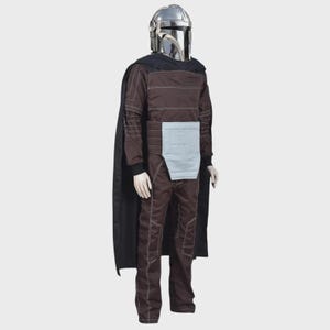 May include: A full-body costume featuring a metallic silver helmet with a T-shaped visor, a dark brown long-sleeved jumpsuit with white contrast stitching, a light gray rectangular waist panel, and a long black cape draped over the shoulders.