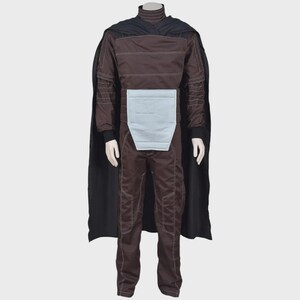May include: A dark brown jumpsuit featuring a high collar, long sleeves with white topstitching, and a light blue rectangular panel at the waist. A long black cape is attached at the shoulders, draping down the back of the full-body garment.