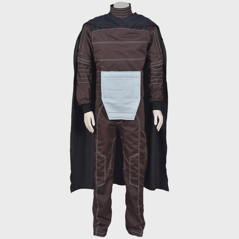 May include: A dark brown jumpsuit featuring a high collar, long sleeves with white topstitching, and a light blue rectangular panel at the waist. A long black cape is attached at the shoulders, draping down the back of the full-body garment.