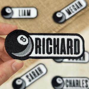 May include: Embroidered patches featuring a black and white 8-ball design with personalized names. The patches have a white background with black text, and a black border. Names include "Richard", "Liam", "Megan", "Sarah", and "Charles".