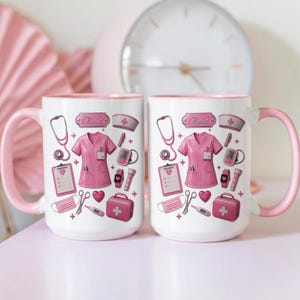 Könnte beinhalten: Zwei weiße Keramiktassen mit rosa Henkeln und Rändern, die ein wiederkehrendes Muster aus medizinischen Illustrationen zeigen, darunter ein rosa Kasack, ein Stethoskop, ein Klemmbrett, eine medizinische Tasche und der Name Olivia auf einem Schild.