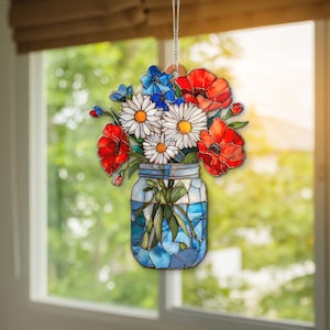 Könnte beinhalten: Ein Fensterbehang aus Buntglas mit einem Blumenstrauß aus roten Mohnblumen, weißen Gänseblümchen und blauen Blumen in einem blauen Einmachglas. Das Glas wird von einer silbernen Kette gehalten, ideal für einen floralen Akzent an jedem Fenster.