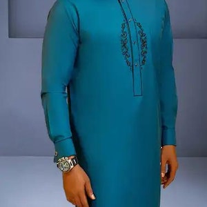 May include: Teal long-sleeve tunic and trousers. The tunic has a mandarin collar and black embroidered detailing. A silver watch with a black strap is visible on the left wrist. The outfit is made of a smooth, solid-coloured fabric.