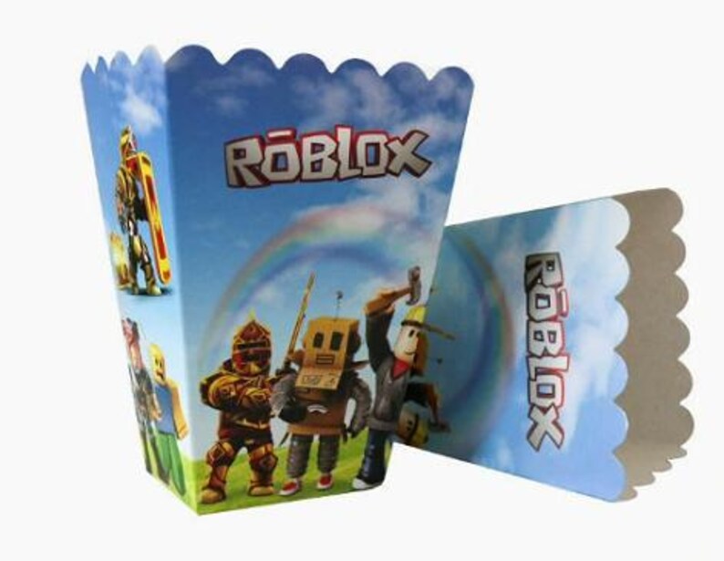 Puede incluir: Una caja de palomitas de papel con un fondo de cielo azul, un arco&iacute;ris y el logotipo de Roblox. La caja muestra varias figuras de personajes del juego, incluido un personaje tipo robot y una figura con un casco amarillo.