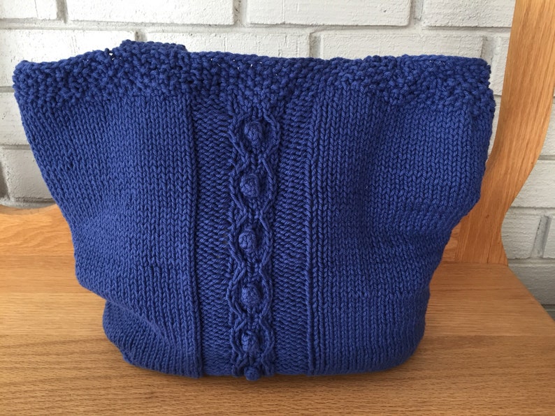 May include: A blue knitted tote bag with a cable knit design and a textured stitch pattern.