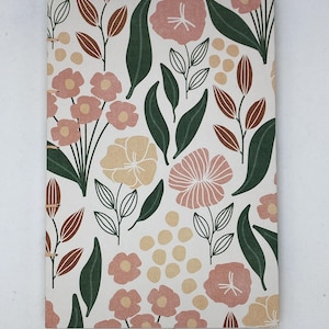 May include: A white notebook with a floral pattern in shades of pink, green, and brown. The flowers are stylized and the leaves are long and thin.