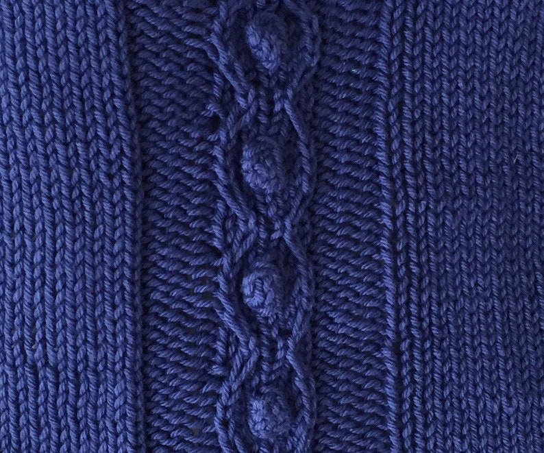 May include: A close-up of a blue knitted fabric with a cable knit pattern and decorative buttons.