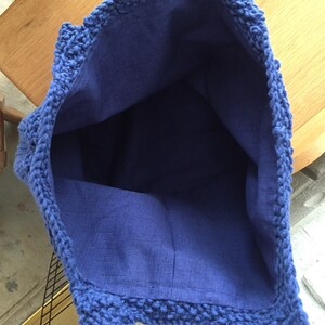 May include: A blue crocheted tote bag with a blue fabric lining. The bag has a wide opening and two handles.