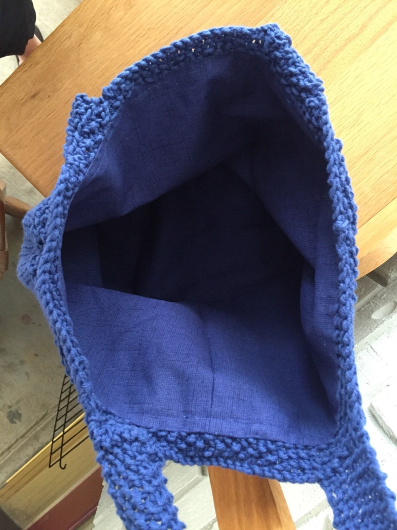 May include: A blue crocheted tote bag with a blue fabric lining. The bag has a wide opening and two handles.