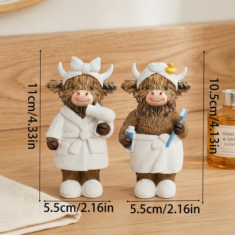 May include: Two Highland cow figurines, each approximately 4.33 inches tall and 2.16 inches wide. One cow wears a robe and holds a hairdryer, the other a towel and toothbrush. Both have white headbands.