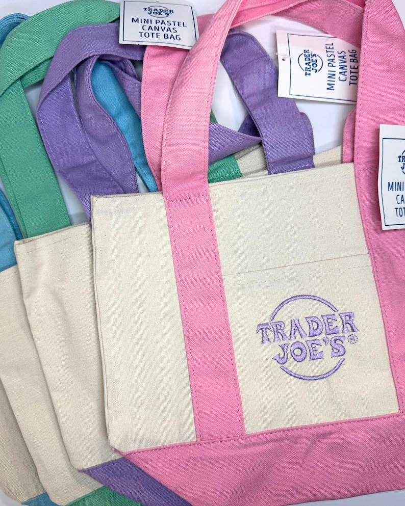 May include: Mini pastel canvas tote bags in shades of pink, purple, green, and blue. Each bag has a cream-colored body with a colored bottom and handles. The Trader Joe's logo is embroidered on the front.