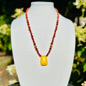 May include: A yellow gemstone pendant necklace with red beads and gold accents.