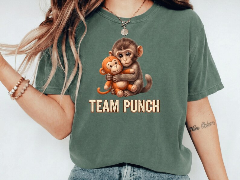 May include: Green t-shirt featuring a graphic of two cartoon monkeys hugging. The text "TEAM PUNCH" is printed below the monkeys in a tan color. The shirt is a solid green color.