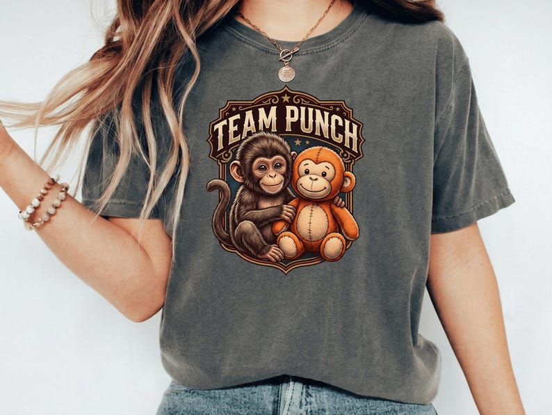 May include: Gray t-shirt featuring a graphic of two cartoon monkeys hugging, with the text "TEAM PUNCH" in a decorative emblem. The monkeys are brown and orange, and the emblem is brown and gold.
