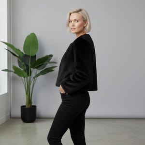May include: A black faux fur jacket with a cropped silhouette. The jacket has long sleeves and a soft, textured appearance. The model is wearing black jeans.