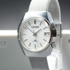 May include: A silver Citizen Tuning Fork Hisonic watch with a white face and a mesh strap. The watch face displays the date as the number 29. The watch has a silver bezel and a silver mesh strap.