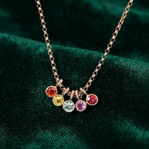 Pode incluir: Um colar dourado com uma corrente delicada. O colar apresenta seis pedras preciosas redondas e coloridas em tons de vermelho, laranja, amarelo, azul, rosa e vermelho. As pedras são engastadas em engastes dourados individuais.