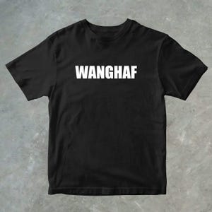 Puede incluir: Camiseta negra con la palabra "WANGHAF" impresa en letras blancas mayúsculas en el pecho. La camiseta tiene cuello redondo y mangas cortas. La tela parece suave.