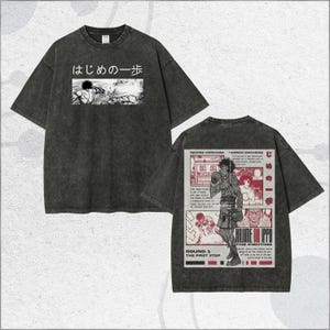 May include: Dark gray t-shirt featuring Japanese text and a black and white manga illustration on the front. The back of the shirt displays a red and white manga-style graphic with a boxing theme. The shirt has a vintage, worn look.