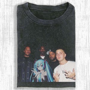 May include: Dark grey t-shirt with a graphic featuring Dr. Dre, Snoop Dogg, Ice Cube, Eminem, and an anime character. The design is printed on a pre-washed, vintage-style tee.