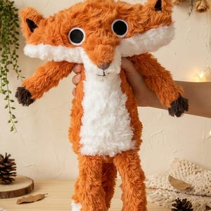 May include: A plush fox toy with orange fur, white chest, and large black eyes. The fox has a long body and outstretched arms, with brown accents on the ears and paws. The toy is soft and cuddly, perfect for children.