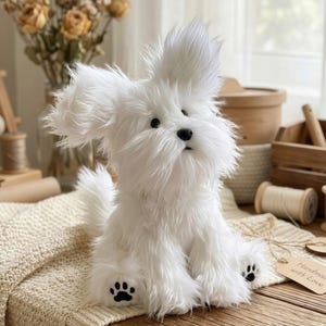 May include: A fluffy white stuffed dog with black paw prints on its feet sits on a cream-colored knitted blanket. The dog has large, upright ears and a black nose. A tag that says "Handmade with Love" is attached.