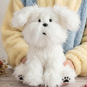 May include: A fluffy white plush dog with black eyes and a black nose. The stuffed animal has a long, shaggy coat and black paw prints on its feet. The dog is sitting upright.