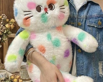 May include: A white plush cat toy with colorful polka dots in shades of pink, orange, green, and purple. The cat has embroidered facial features and pink accents on its ears. The toy is soft and fluffy, with a whimsical design.
