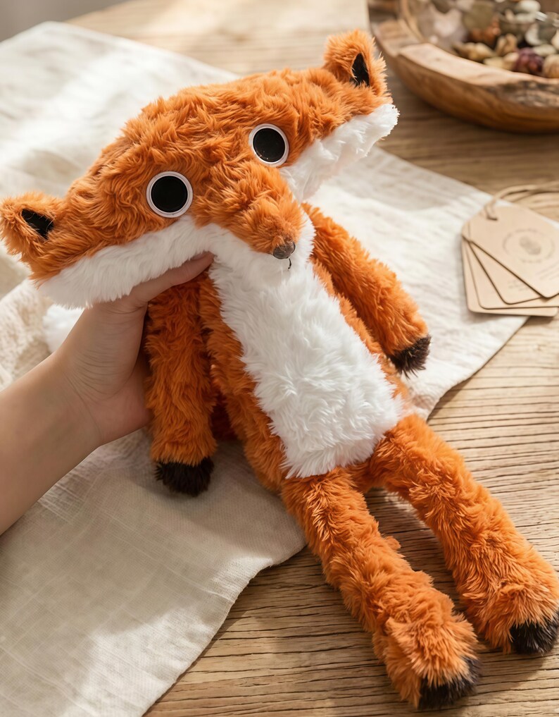 May include: A plush fox toy with orange and white fur, large black eyes, and brown accents on the ears and paws. The stuffed animal is soft and cuddly, perfect for children or as a decorative item.