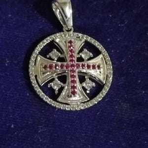 May include: A silver pendant with a Jerusalem cross design. The cross is adorned with red gemstones and surrounded by a circle of clear stones. The pendant has a silver bail for attaching to a chain.