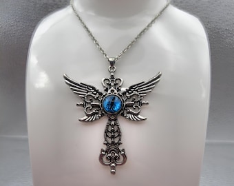 May include: Silver-toned pendant necklace featuring a cross design with ornate detailing and small wings. The center of the cross has a blue, round stone. The necklace is displayed on a white mannequin.