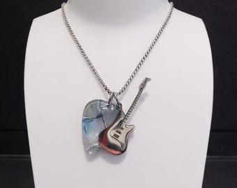 May include: A silver-toned necklace with two pendants. One pendant is a clear heart-shaped piece with blue and white swirls. The other is a miniature electric guitar pendant with a red and silver finish. The necklace is displayed on a white mannequin.