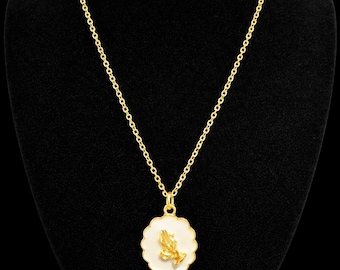 May include: A gold-colored necklace with a pendant featuring praying hands. The pendant is a white scalloped circle with a gold-colored praying hands design in the center. The necklace is displayed on a black mannequin.